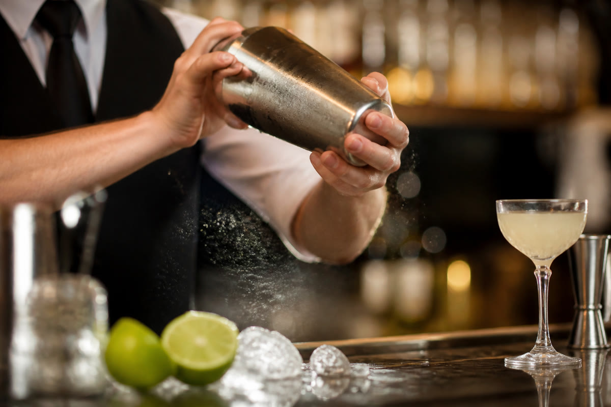 Barman secouant un shaker avec des citrons verts et des glaçons