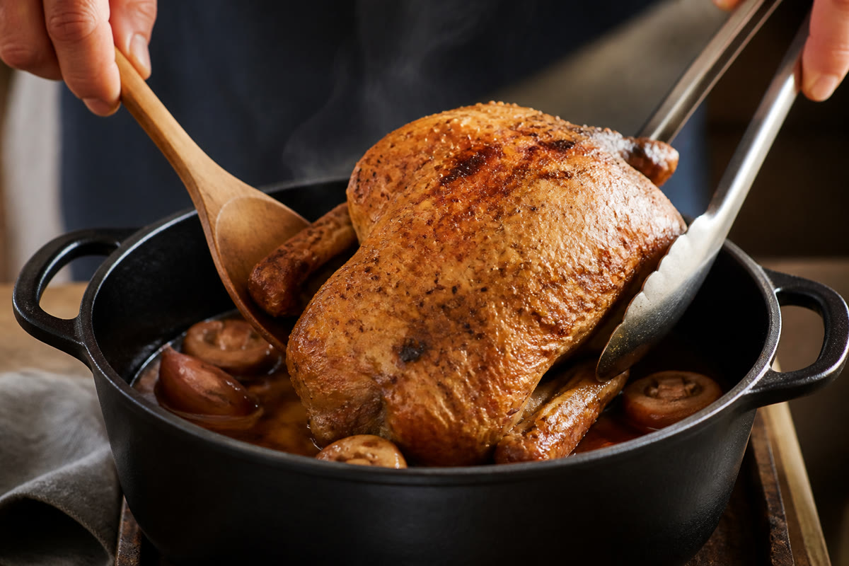Pintade dorée déposée dans une cocotte avec échalotes et champignons