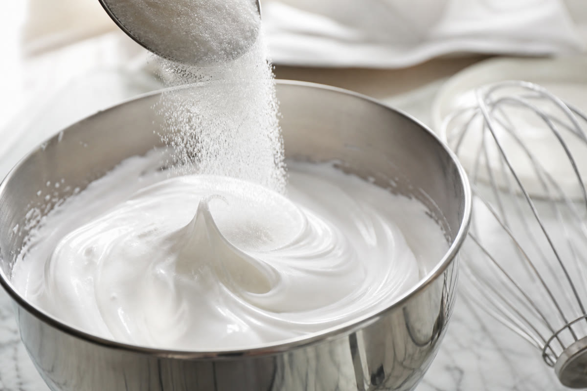 Sucre semoule versé progressivement dans une meringue brillante