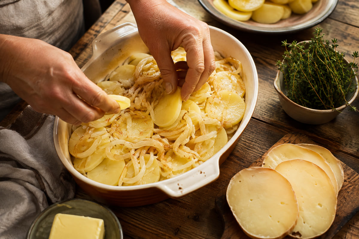 Mains répartissant des pommes de terre précuites et des oignons fondus dans un plat à gratin